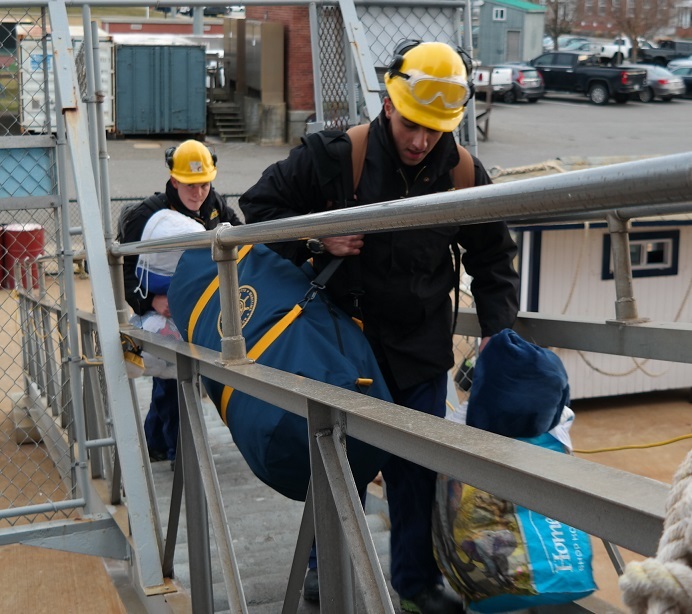 cadets carry sea bags onto ship