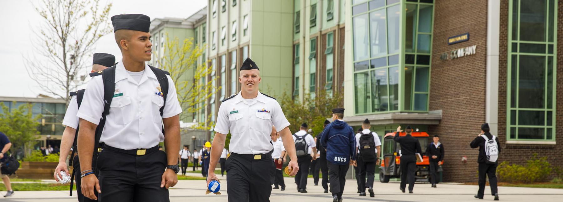 cadets in uniform walking along area outside of dorms